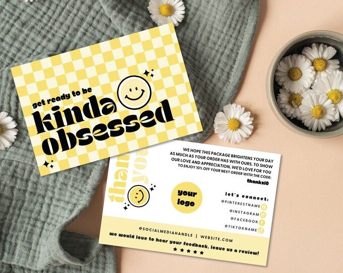 a yellow and white business card sitting on top of a table next to some daisies