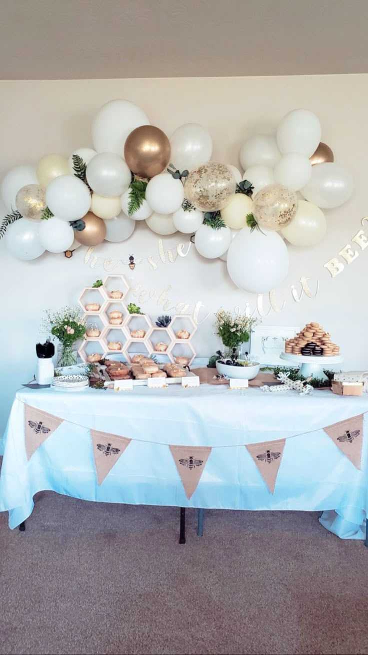 a table topped with lots of balloons and desserts next to a wall filled with honeycombs