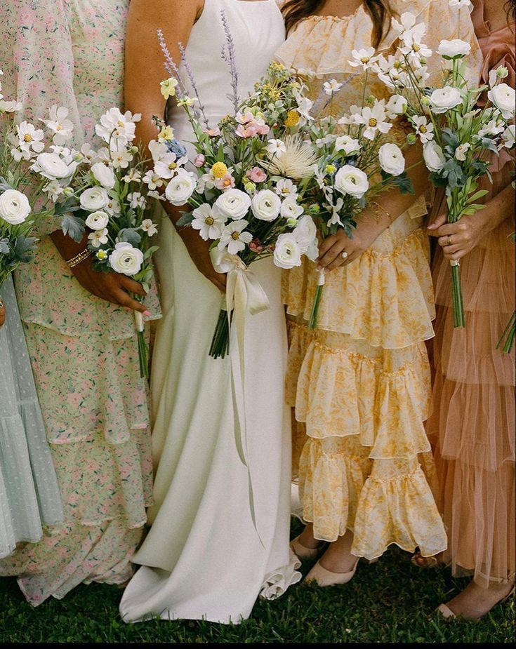 a group of women standing next to each other in dresses and holding bouquets with flowers