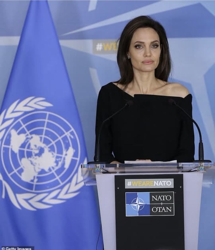 a woman standing at a podium in front of two flags and an un flag behind her