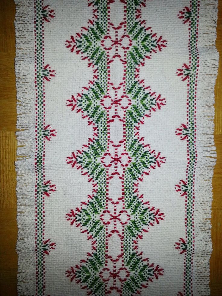 a white table cloth with red and green designs on the edges, sitting on a wooden surface