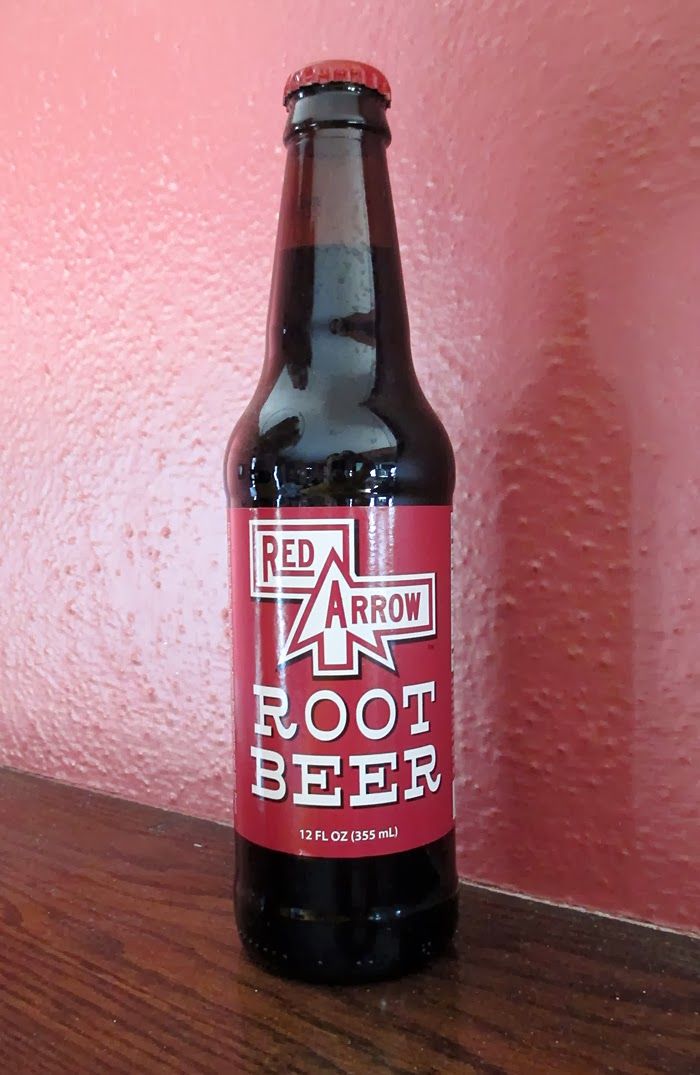 a bottle of root beer sitting on top of a wooden table next to a pink wall