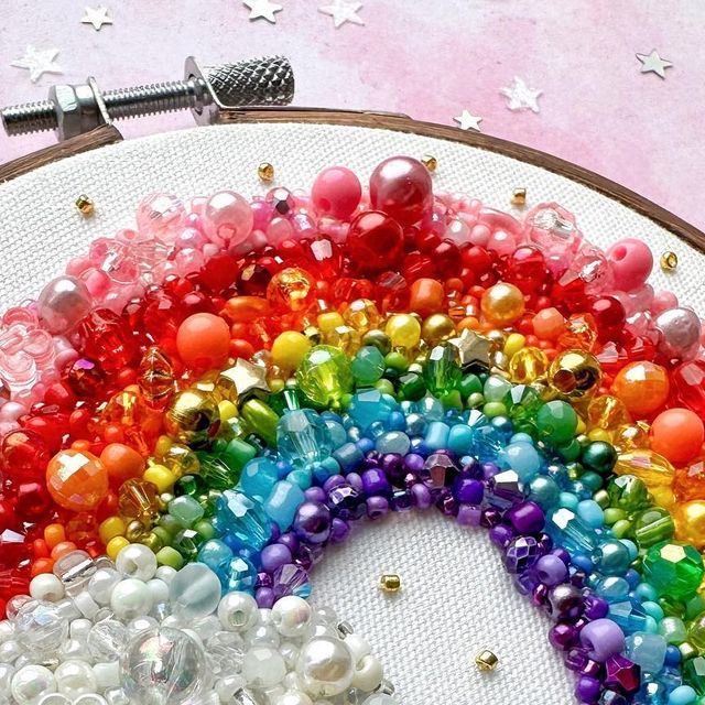 a rainbow made out of glass beads and pearls on a hoop with a needle in the middle