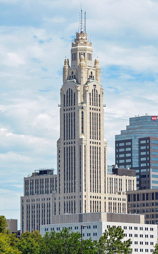 a very tall building with a clock on it's side in front of other buildings