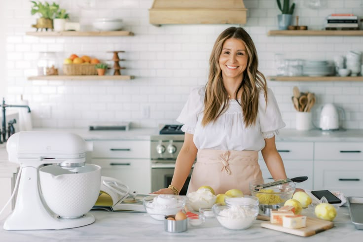 a woman standing in front of a counter with food on it and an appliance behind her