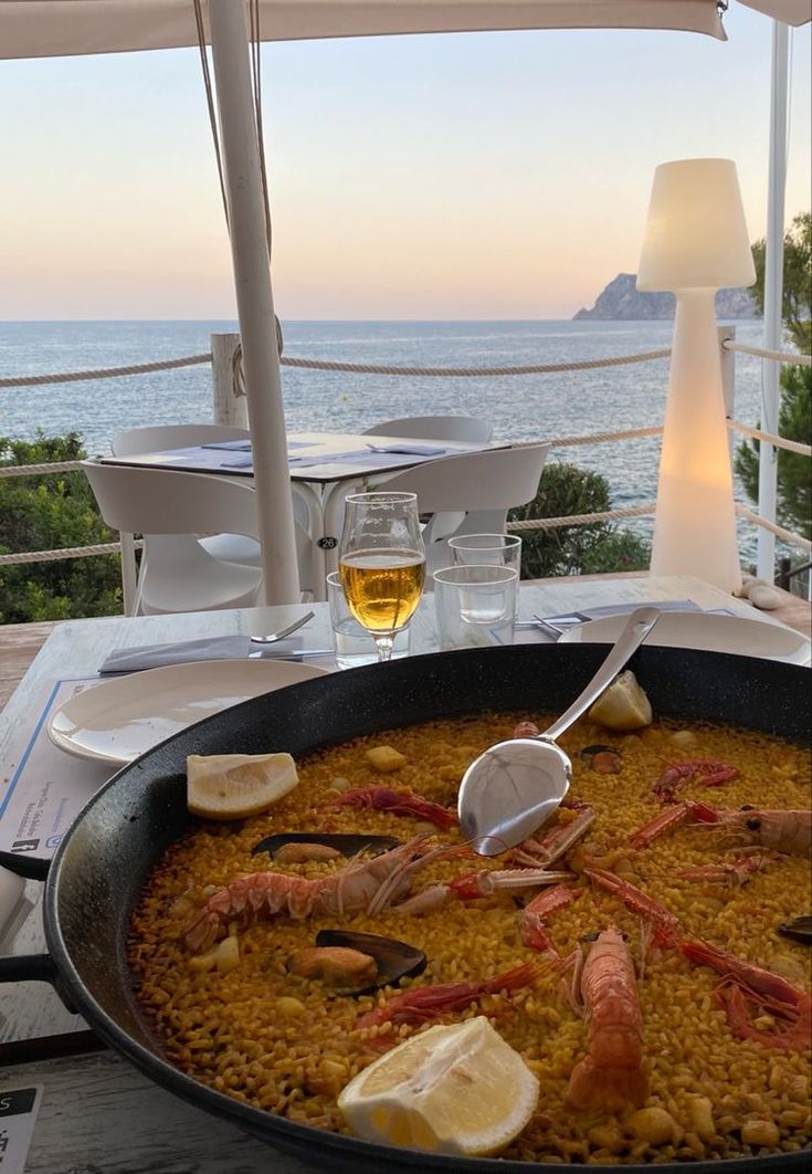 a large pan filled with food on top of a wooden table next to the ocean