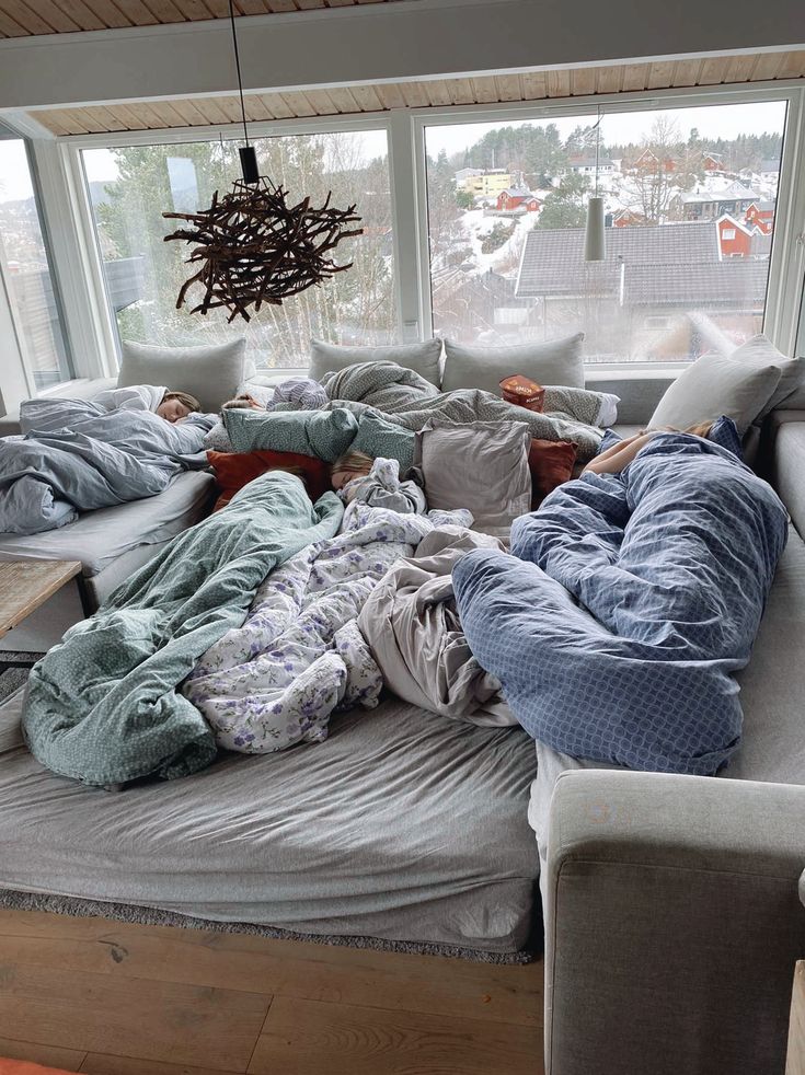 an unmade bed in front of a large window with lots of blankets on it