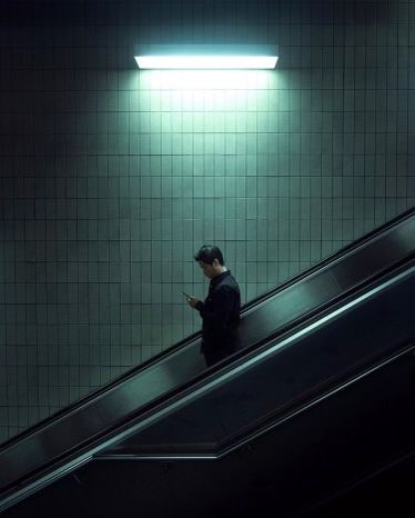 a man on an escalator looking at his cell phone in the dark,