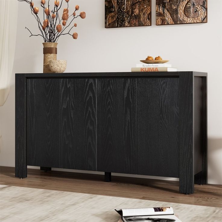 a black sideboard sitting on top of a wooden floor next to a vase filled with flowers