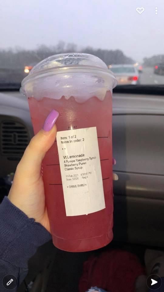 a person holding up a plastic cup filled with liquid in the back seat of a car