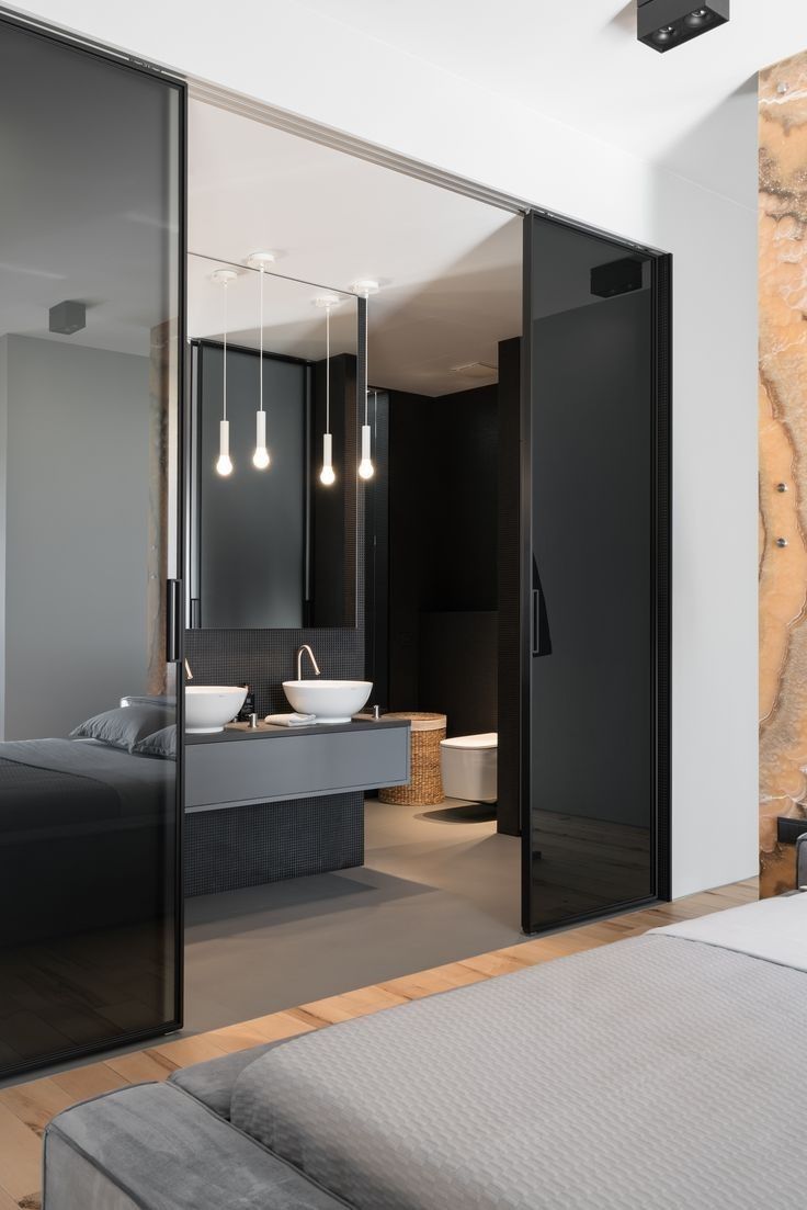 an open bathroom with black glass doors and white walls, along with a large bed in the foreground