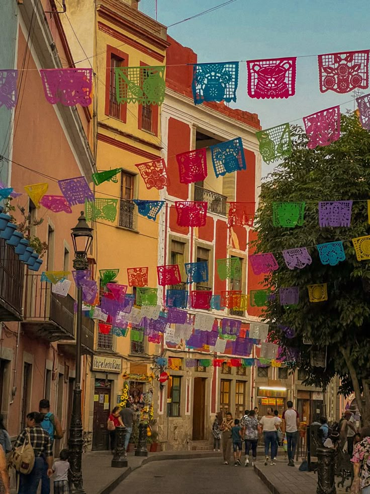 people walking down the street in front of buildings with colorful flags hanging above them and on poles