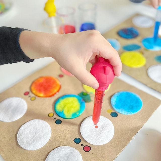 a child's hand is painting circles on paper with colored paint and watercolors