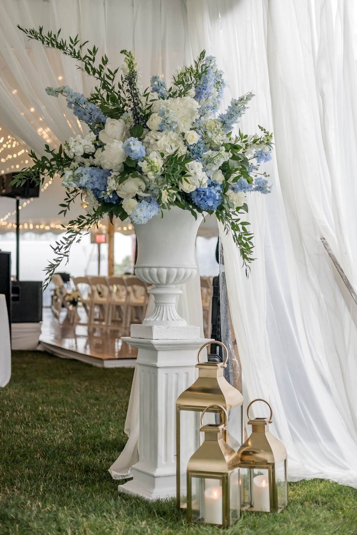 a white vase filled with blue and white flowers on top of a lush green field