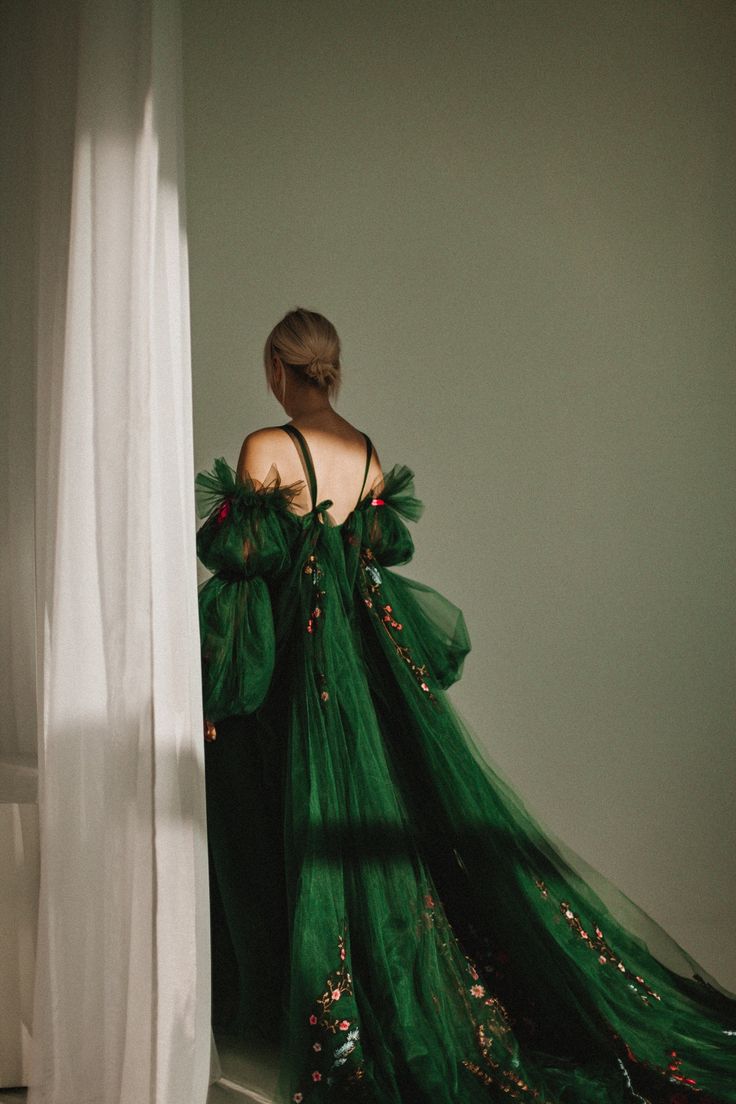 a woman in a green dress is looking out the window with her back to the camera