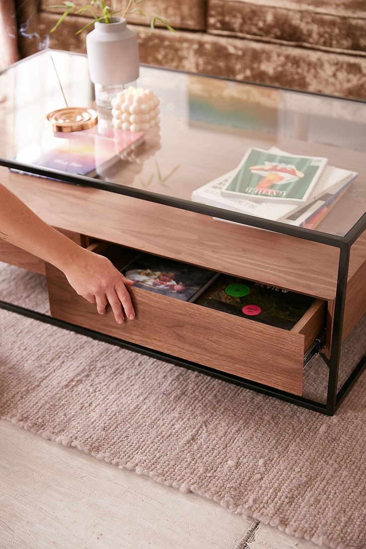 a coffee table with magazines on it and a person's hand reaching into the drawer