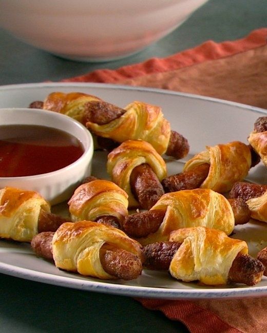 a white plate topped with pigs in a blanket next to a bowl of dipping sauce