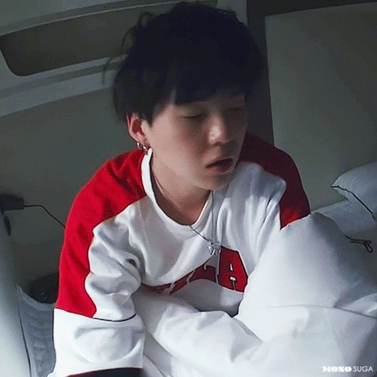 a young man sitting on top of a bed wearing a red and white jacket with his hands folded over his chest