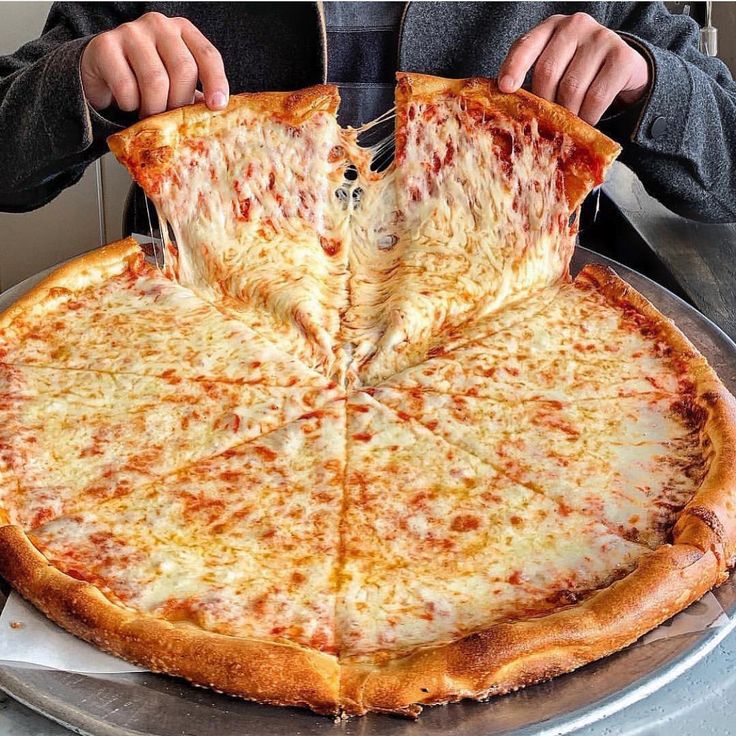 a person cutting into a large pizza on top of a metal pan with one slice taken out