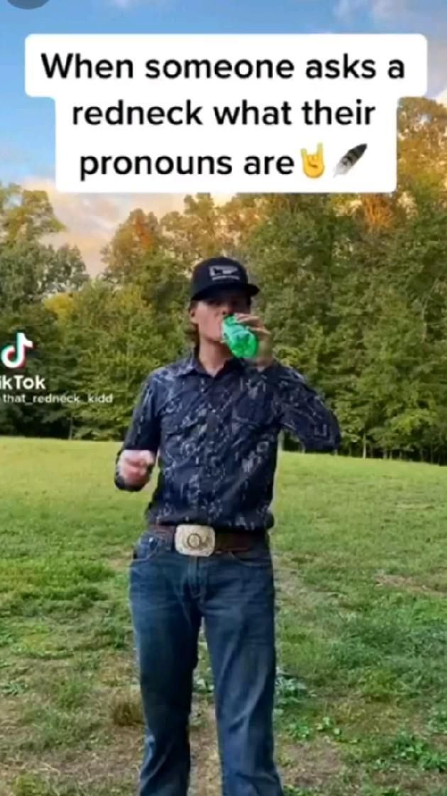 a man standing on top of a lush green field holding a bottle of beer in his hand