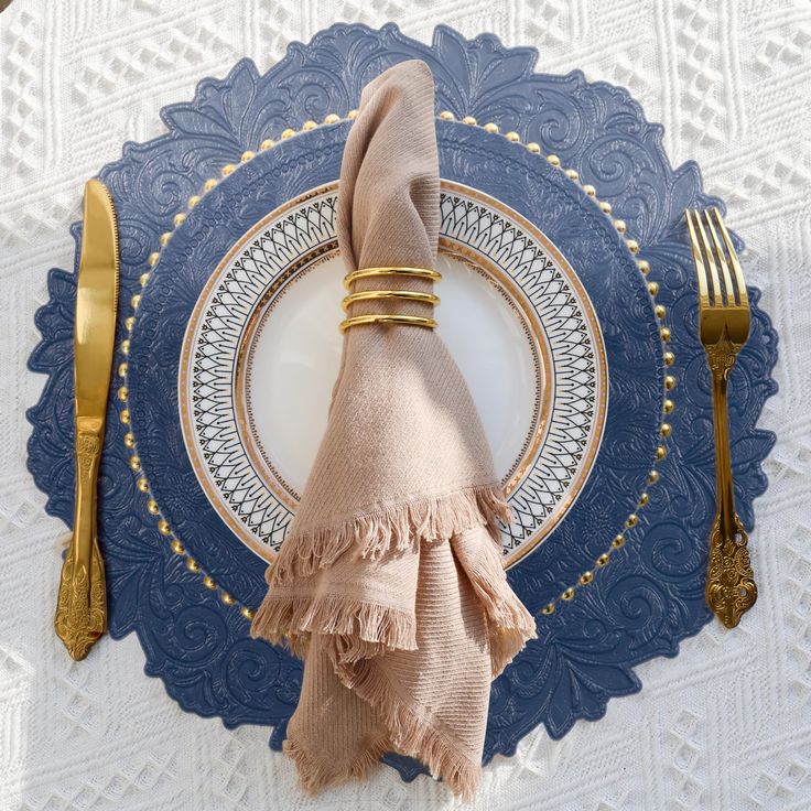 a place setting with napkins and goldware on a blue lace doily,