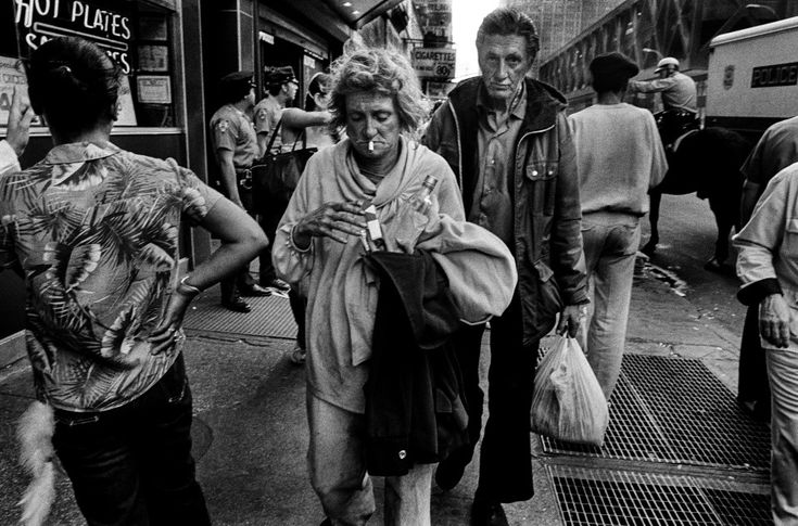 black and white photograph of people walking on the sidewalk in front of a bus stop