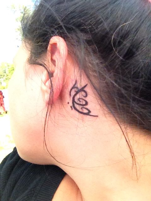 the back of a woman's neck with a small tattoo on her left ear