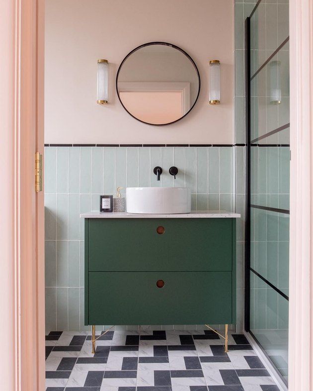 a bathroom with black and white checkered flooring, green cabinets and a round mirror on the wall