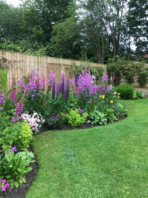 a garden filled with lots of flowers next to a lush green field and wooden fence