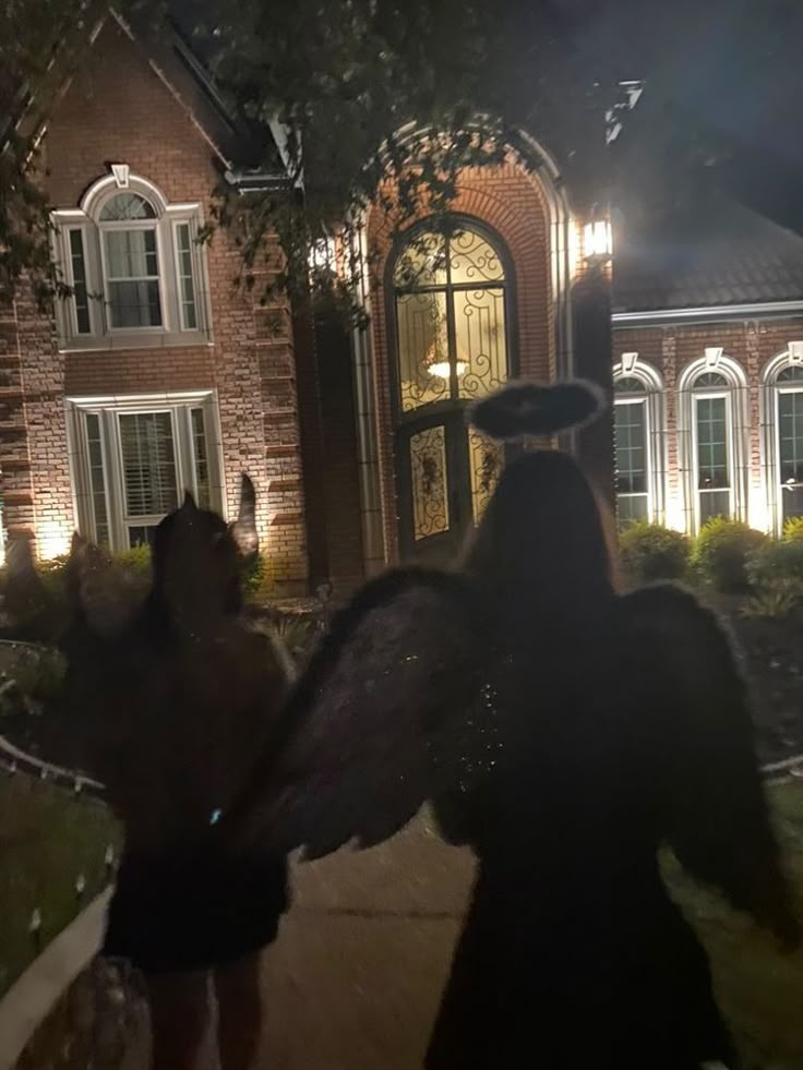 two people in costumes are walking towards a house at night with lights shining on the windows