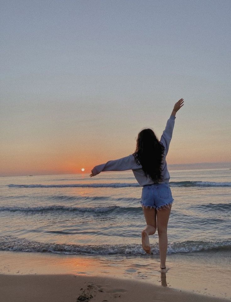 a woman jumping in the air on top of a beach next to the ocean at sunset