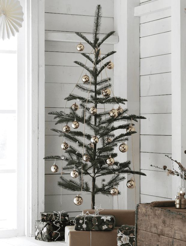 a small christmas tree with gold ornaments and presents under it in front of a white wall