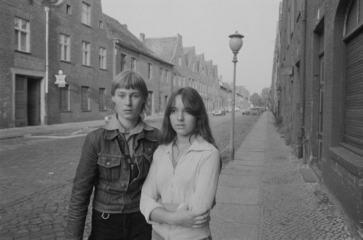 black and white photograph of two people standing next to each other in an alleyway