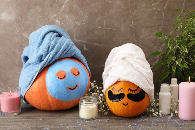 two pumpkins with towels on their heads and candles next to them, one has eyes closed