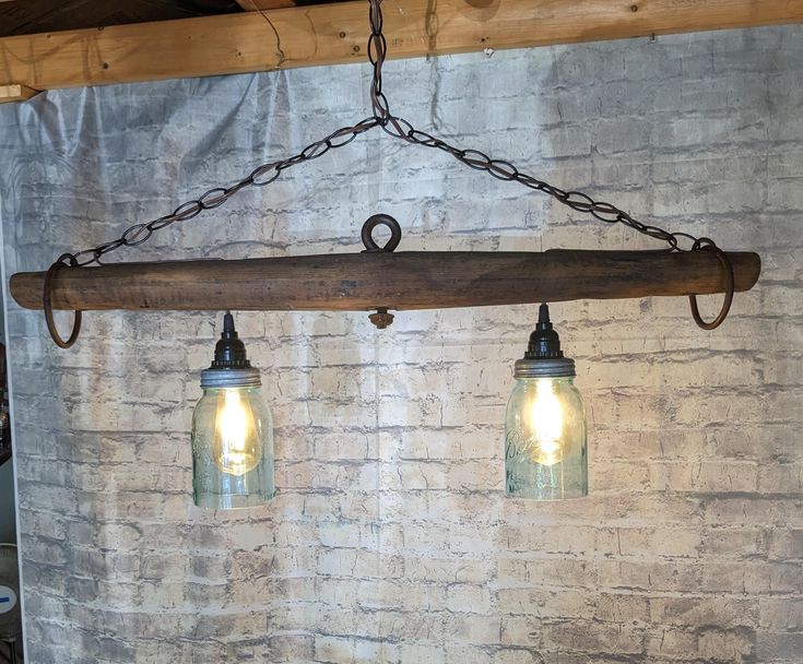 two lights hanging from a wooden beam in front of a white brick wall and metal chain