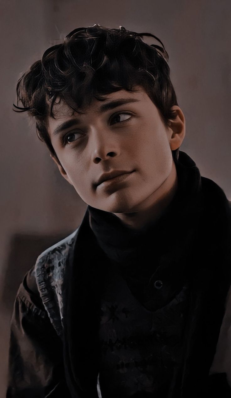 a young man with curly hair and black shirt looks at the camera while posing for a portrait