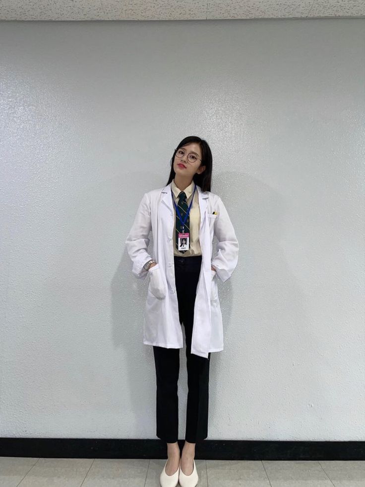 a woman standing in front of a wall wearing a lab coat