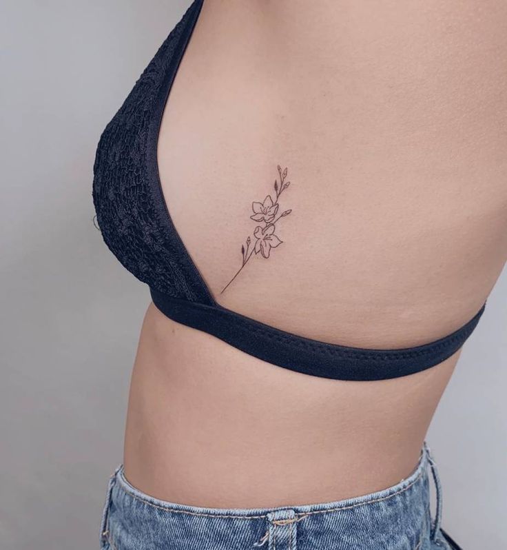 a woman's stomach with a small flower tattoo on her left side ribcage