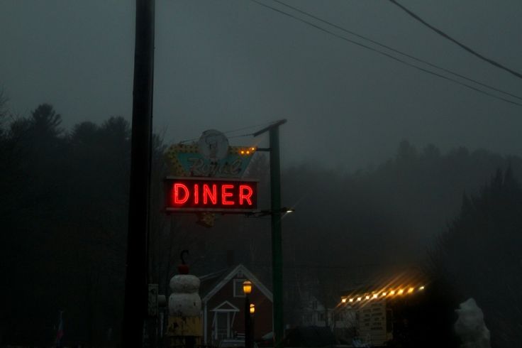 a diner sign lit up in the dark on a foggy day with no one around