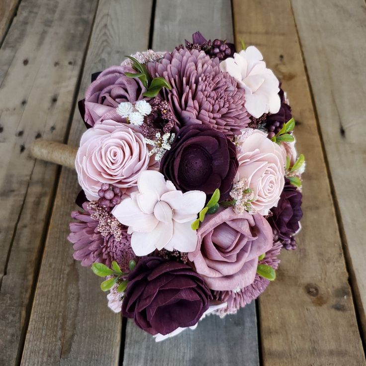 a bridal bouquet with purple and white flowers on a wooden table next to wood planks