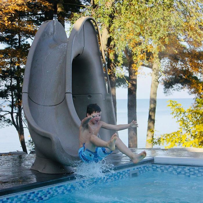 a young boy sliding down a slide into a swimming pool with trees in the background