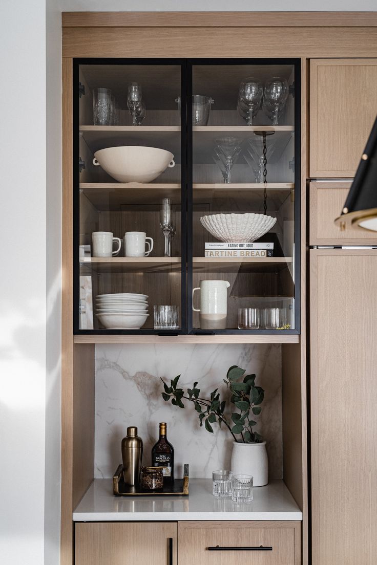 an open cabinet with dishes and cups on the top shelf, in front of a marble countertop