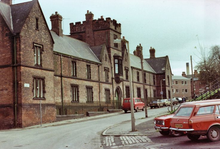 an old red car parked on the side of a road in front of a brick building