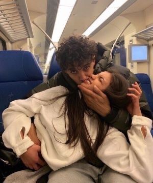 a man and woman sitting on a train kissing each other's foreheads as they sit next to each other