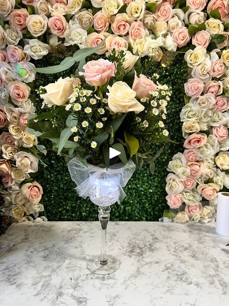 a vase filled with flowers sitting on top of a table next to a wall covered in roses