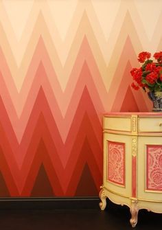 an orange and pink wall with red flowers next to a small table in front of it