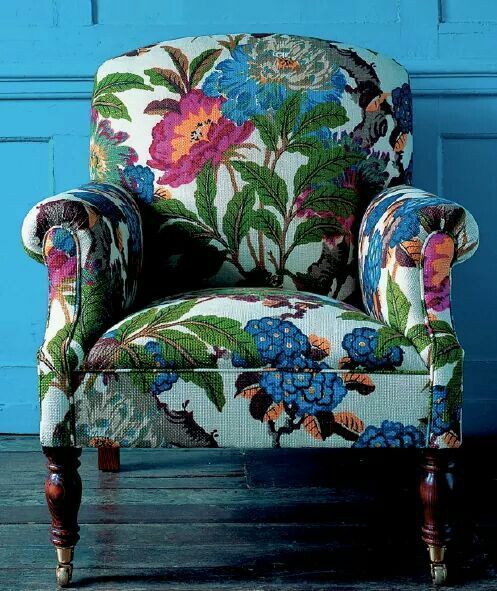 an upholstered chair in front of a blue wall with flowers on the back