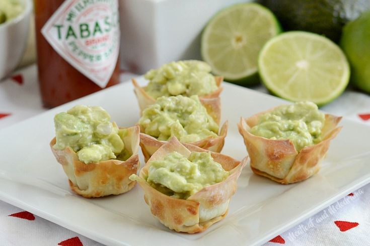 small cups filled with guacamole on a white plate next to limes