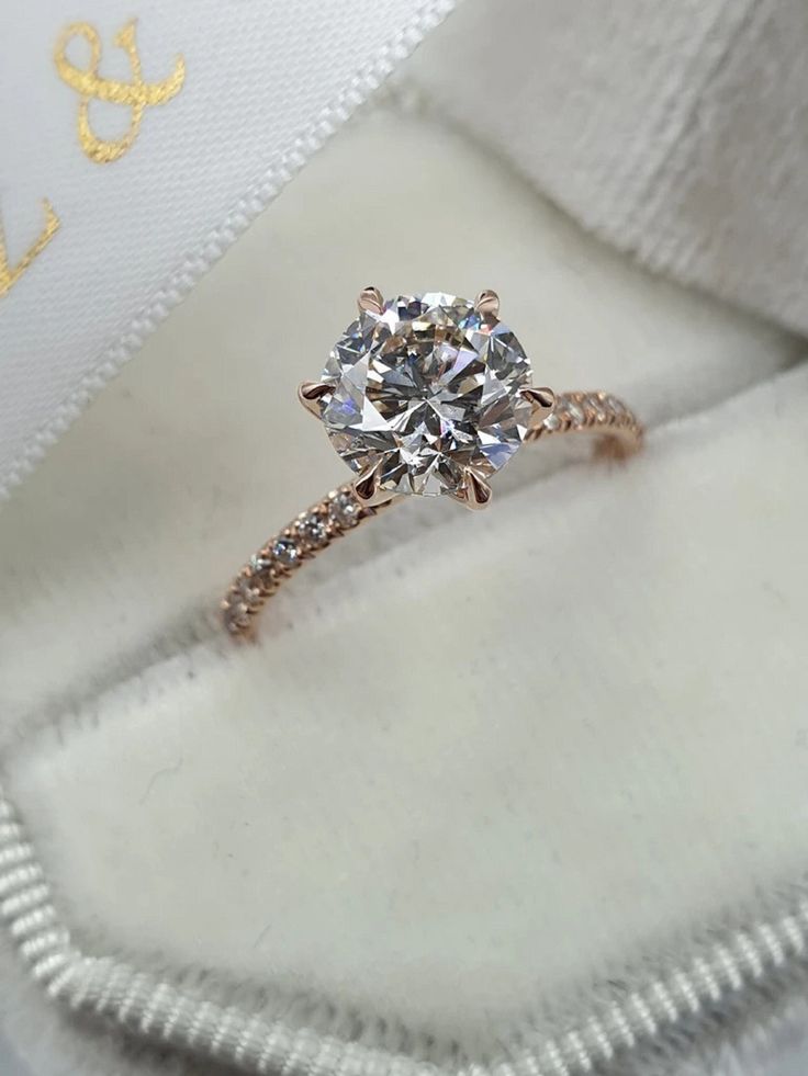 an engagement ring with a diamond on it in a white cloth box and gold lettering