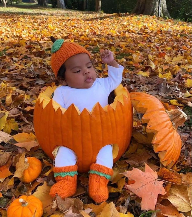 a baby in a pumpkin costume sitting on leaves